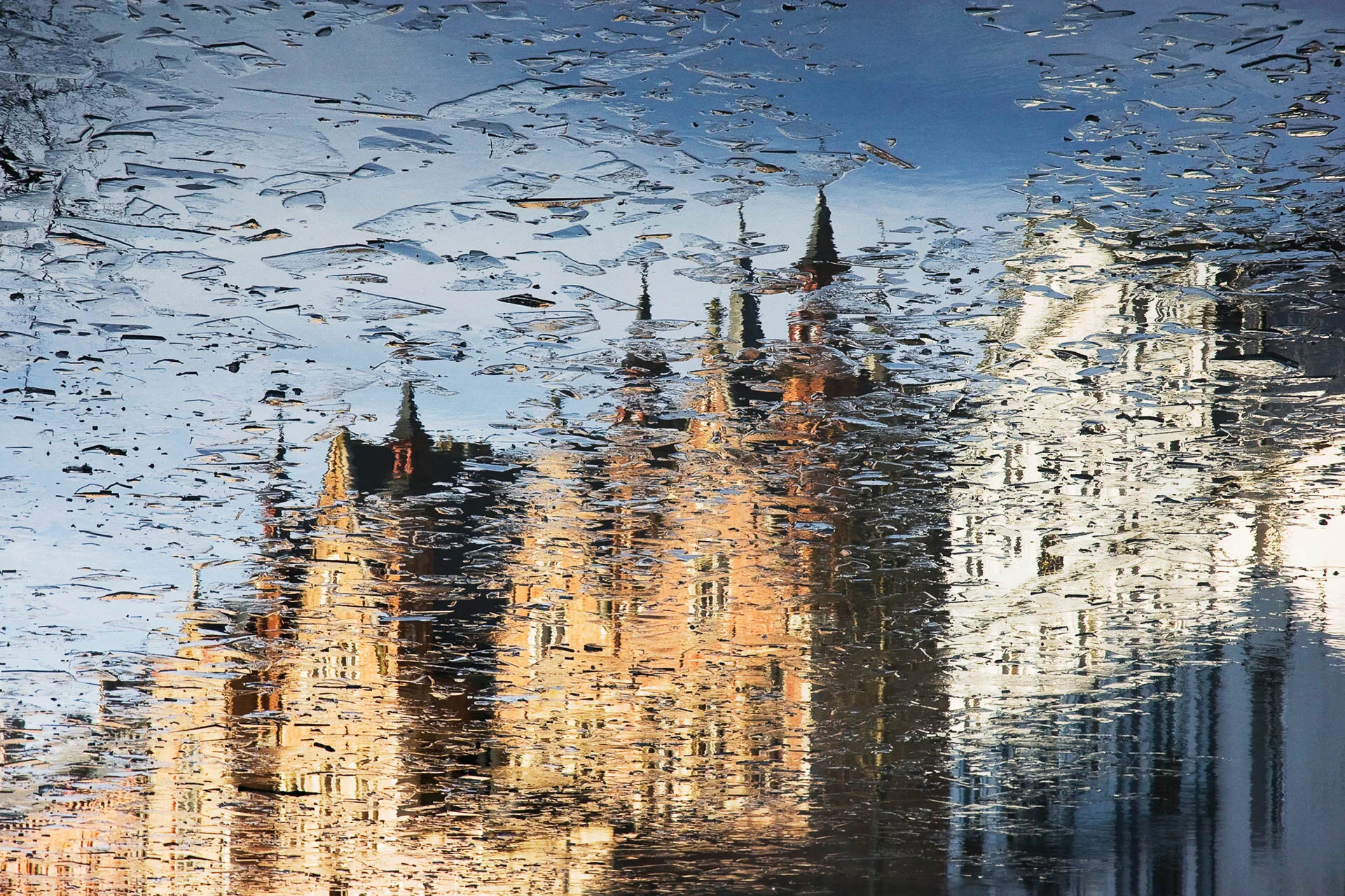 Reflection of a historic building with towers in water with ice patterns.