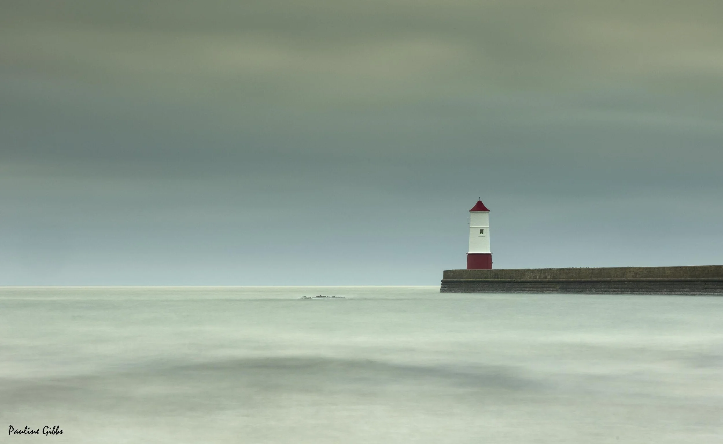 Lighthouse on a pier with calm sea and overcast sky