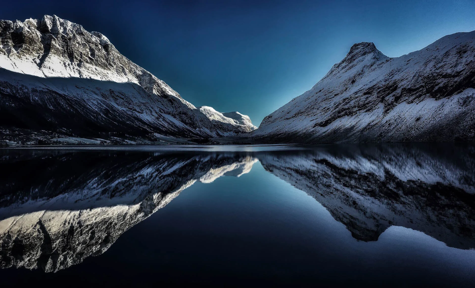 Snow-covered mountains reflected in a calm lake under a clear blue sky.