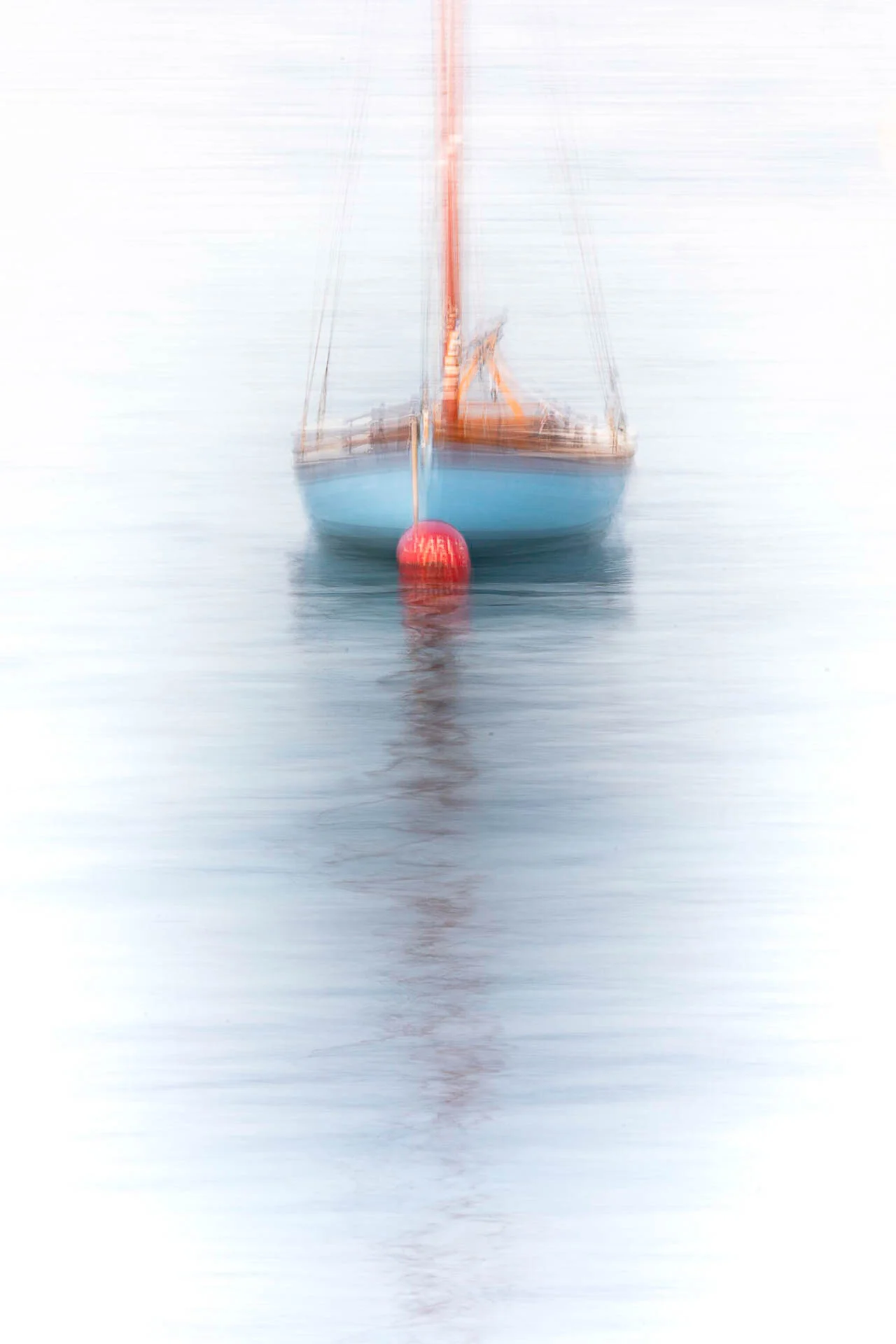 Blurry photo of a sailboat on water with a red buoy in front.