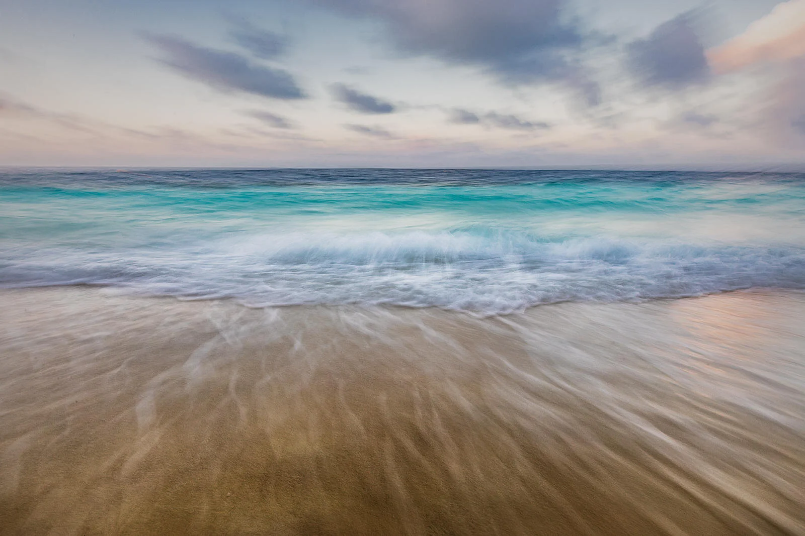 Sandy beach with gentle waves under a cloudy sky