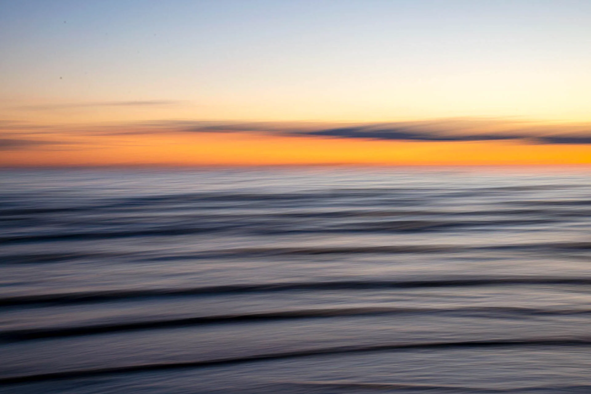 Abstract view of ocean waves at sunset with vibrant orange and blue hues.