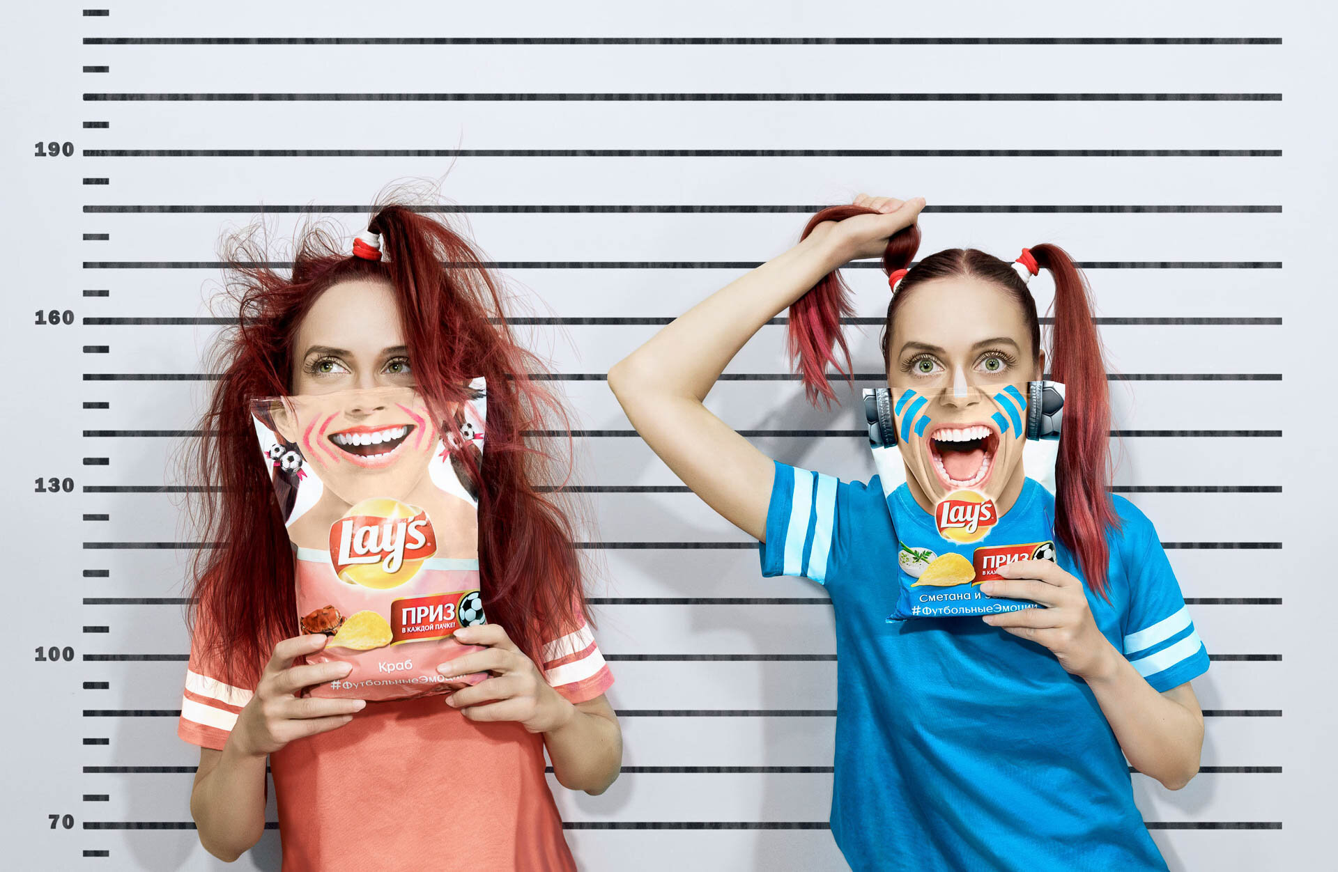 Two women with athletic hairstyles holding Lay's potato chip bags in front of their faces, which blend into the bags. The women are standing against a height chart in a playful manner.