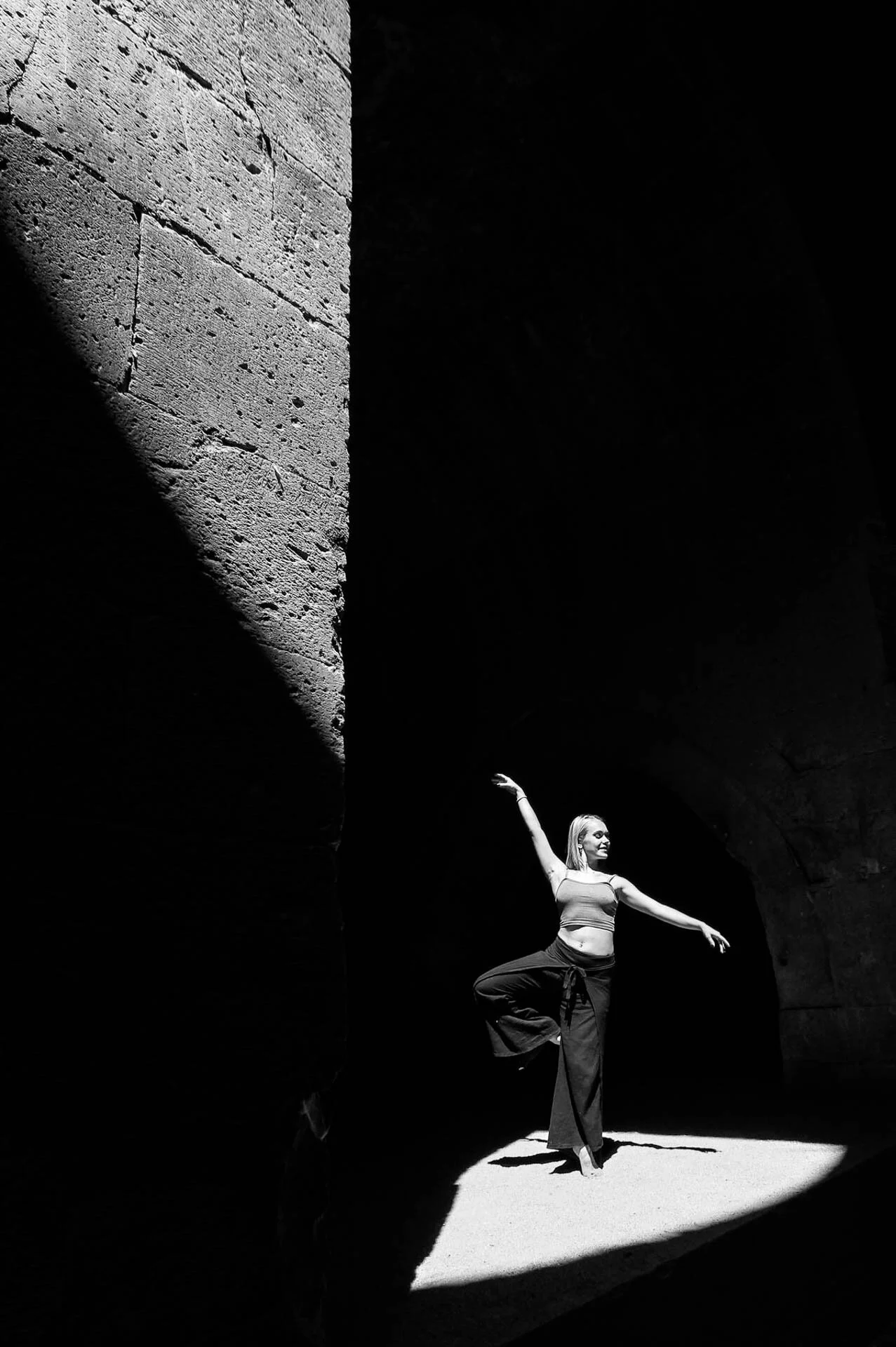 Ballet dancer posing in spotlight against dark background, black and white photo.