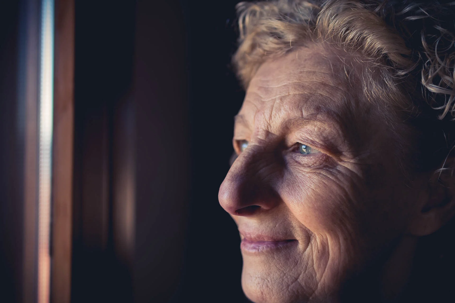 Elderly woman looking out a window with a thoughtful expression
