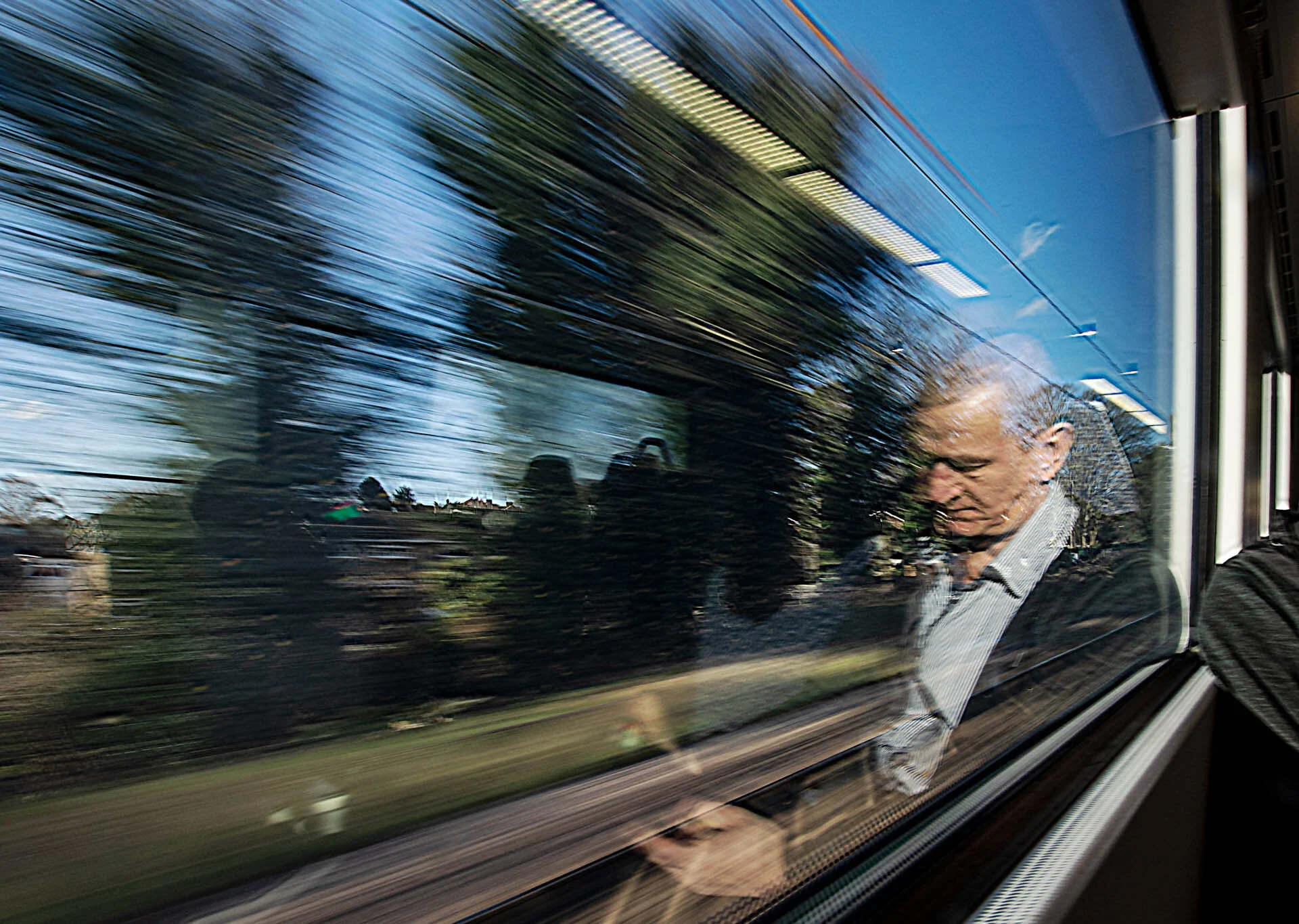A person sitting on a train looking down, with blurred scenery outside the window suggesting movement.