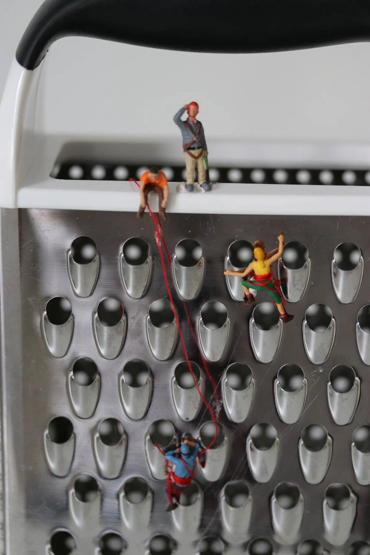 Miniature figures climbing a cheese grater, depicting a mountaineering scene.