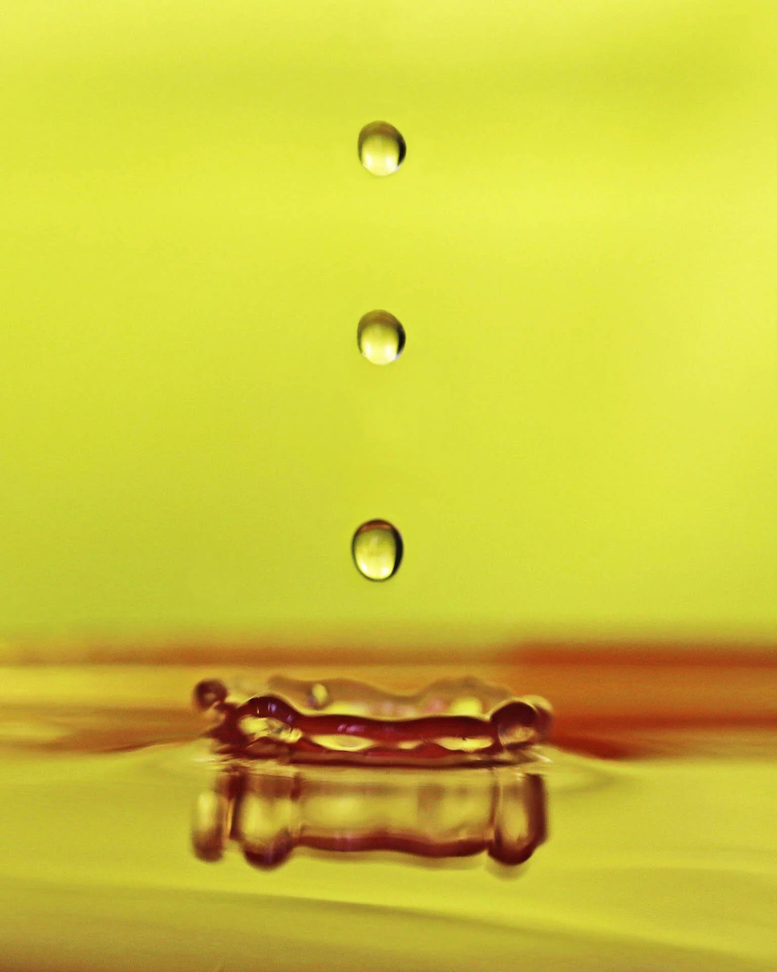 Four water droplets falling into a pool of liquid, creating a splash, against a yellow background.