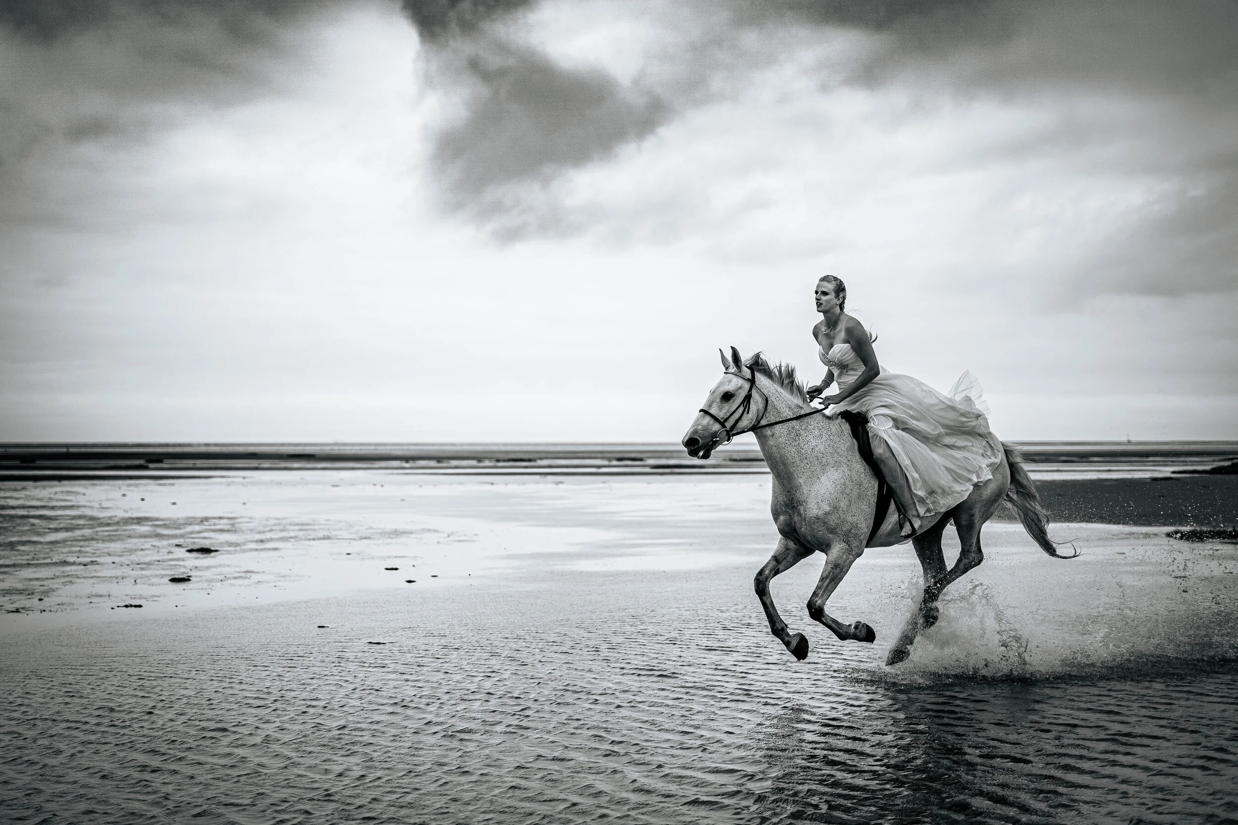 Woman in a wedding dress riding a horse on a beach.