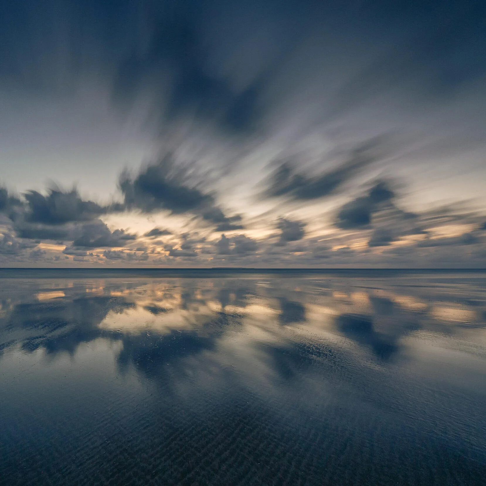 Reflection of clouds on a calm sea at sunset
