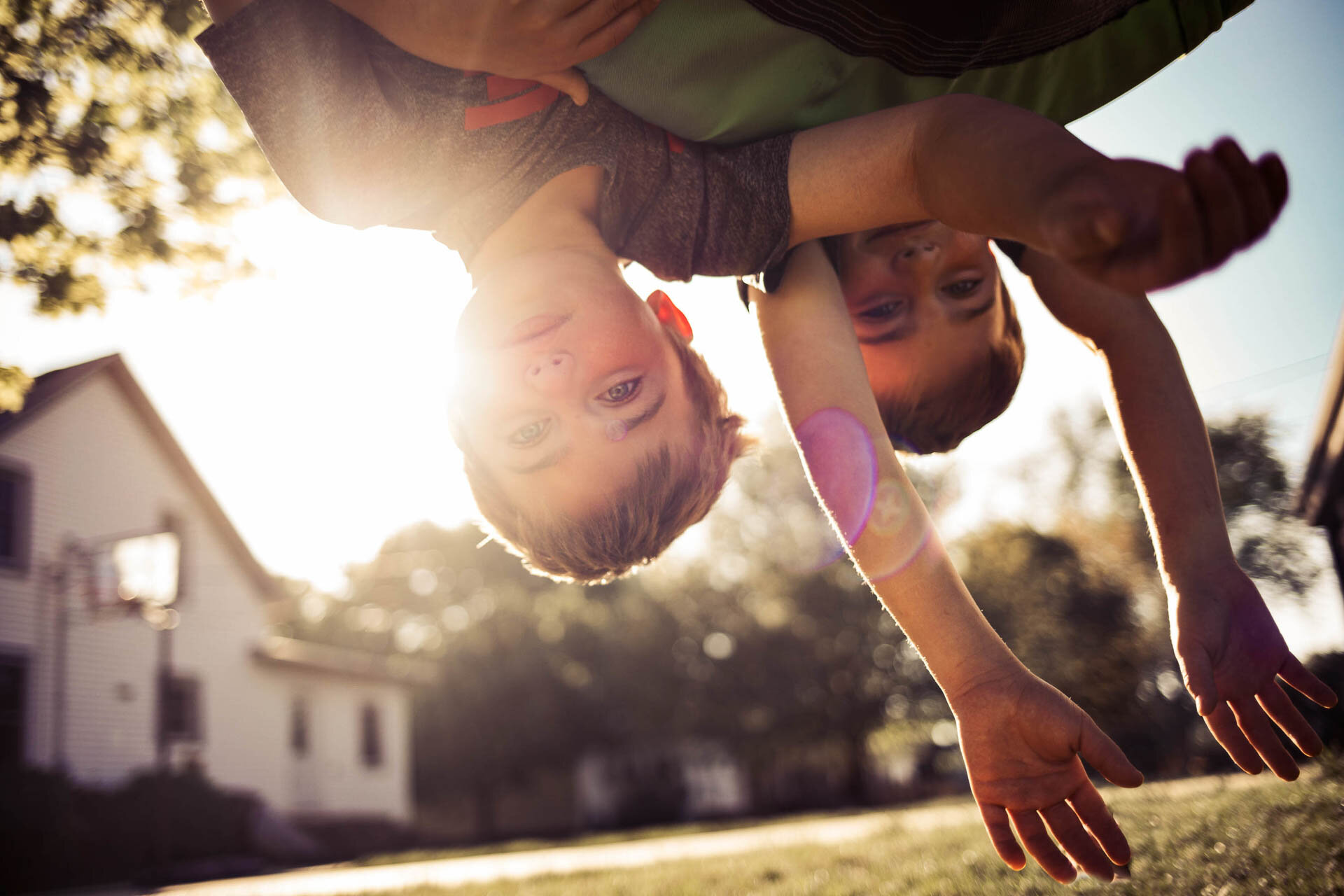 Children playing upside down in front of a house with sun flare