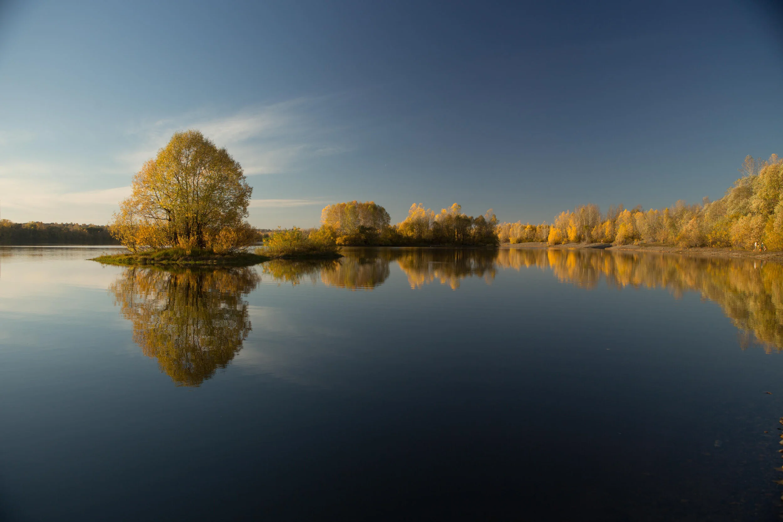 Serene lake scene with autumn trees reflecting in the water, featuring a small island with a tree.