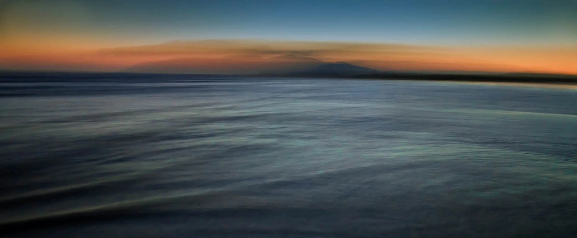 Blurred seascape with a distant mountain, sunset colors and ocean waves.