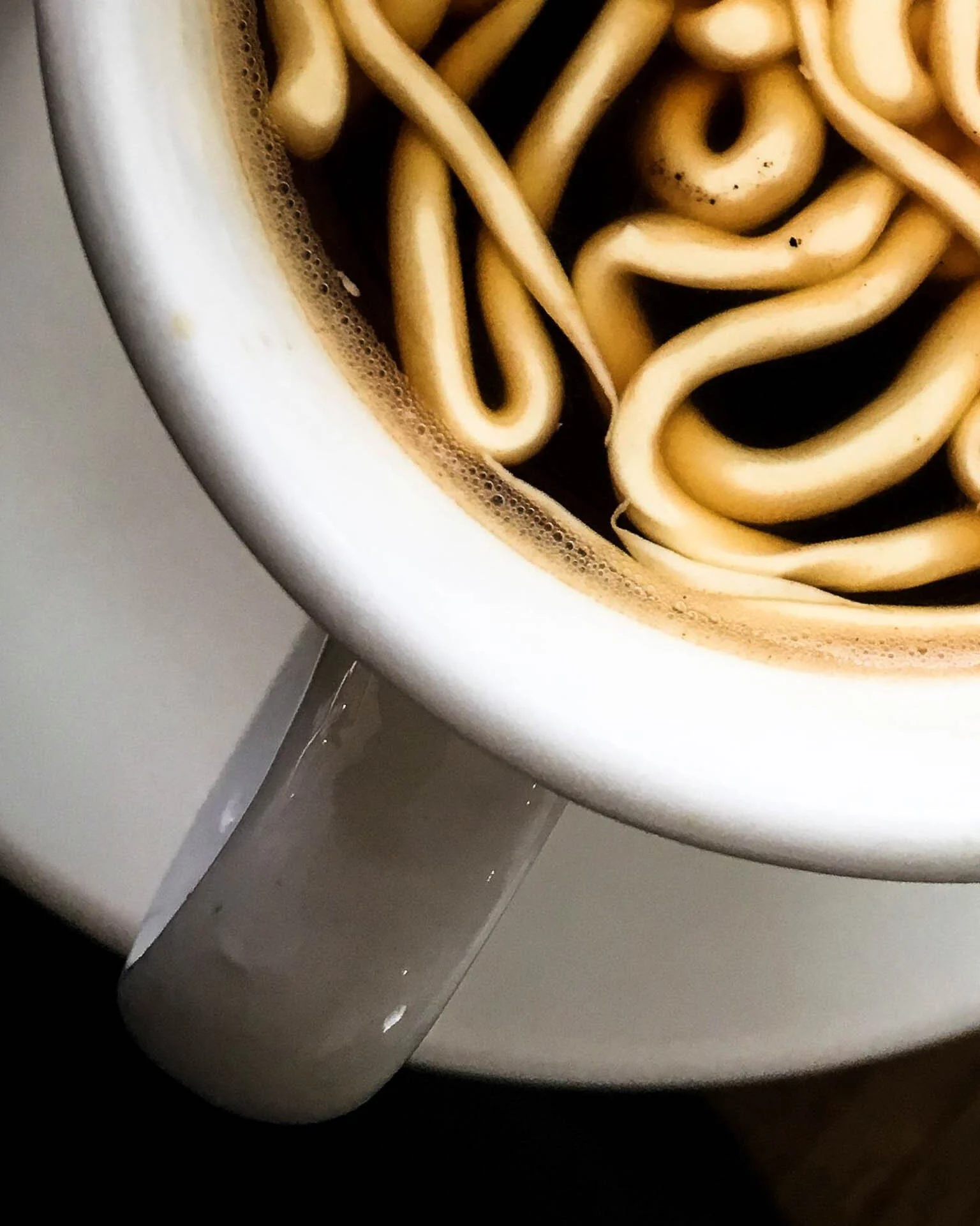 Top view of noodles in a white coffee cup on a saucer.