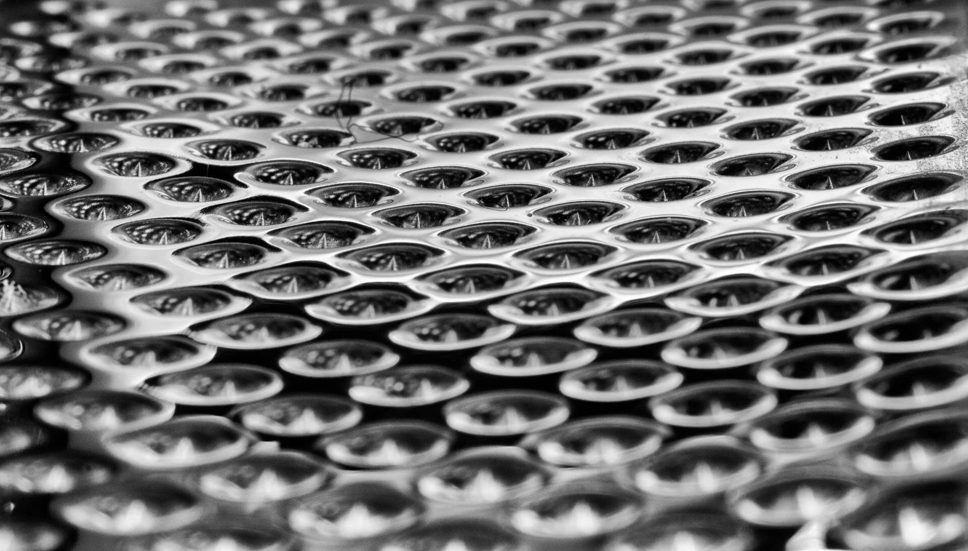 Close-up of a metal surface with a pattern of oval-shaped holes, resembling a cheese grater.