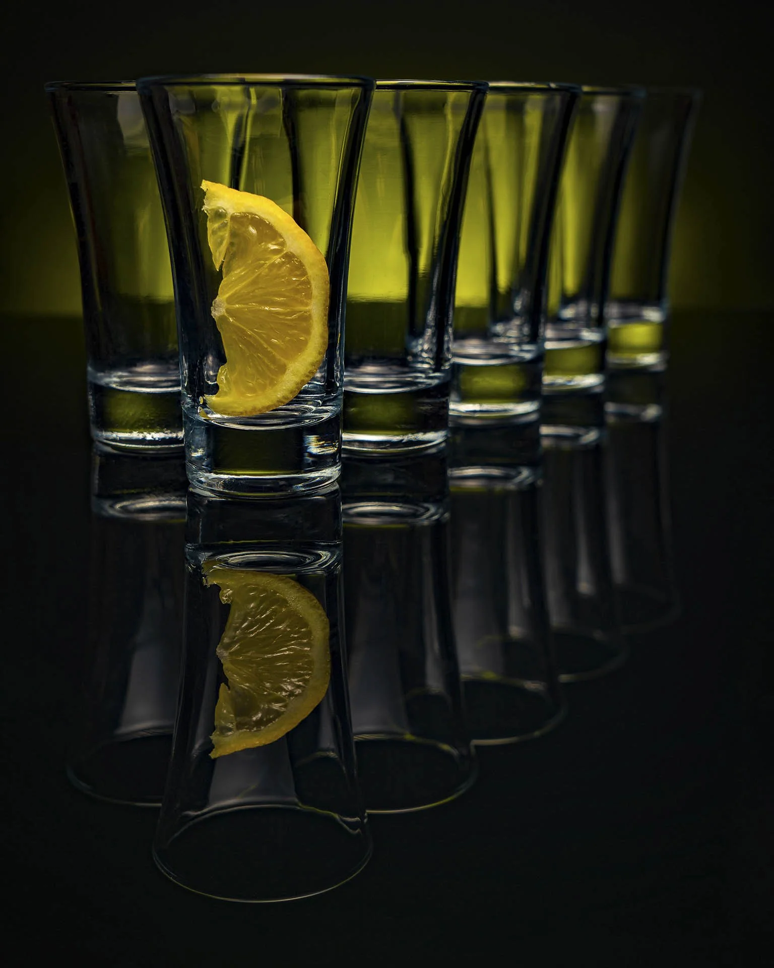 Row of empty shot glasses with a lemon wedge in one glass, reflective surface, dark background