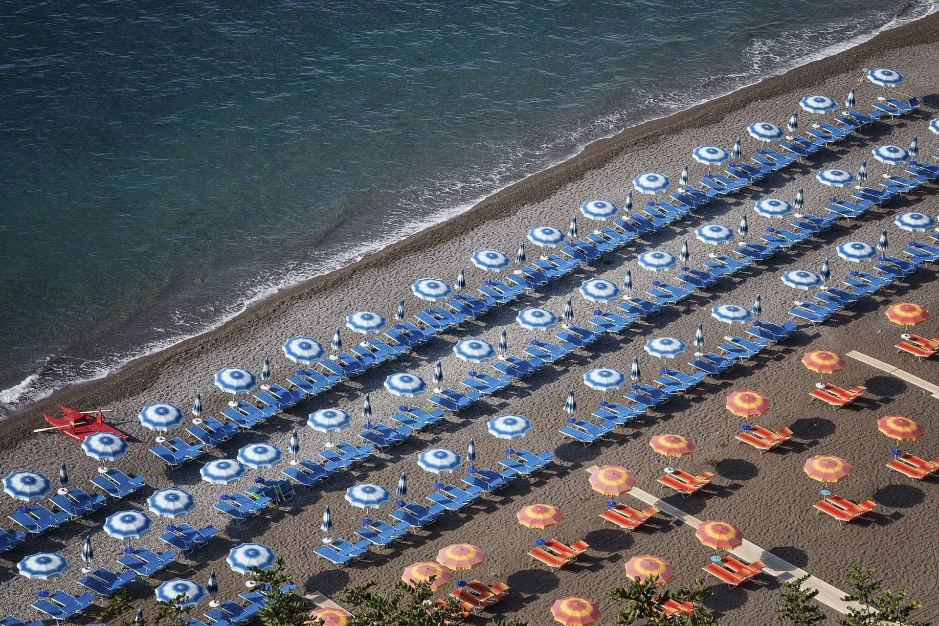 Beach with rows of blue and orange umbrellas and lounge chairs