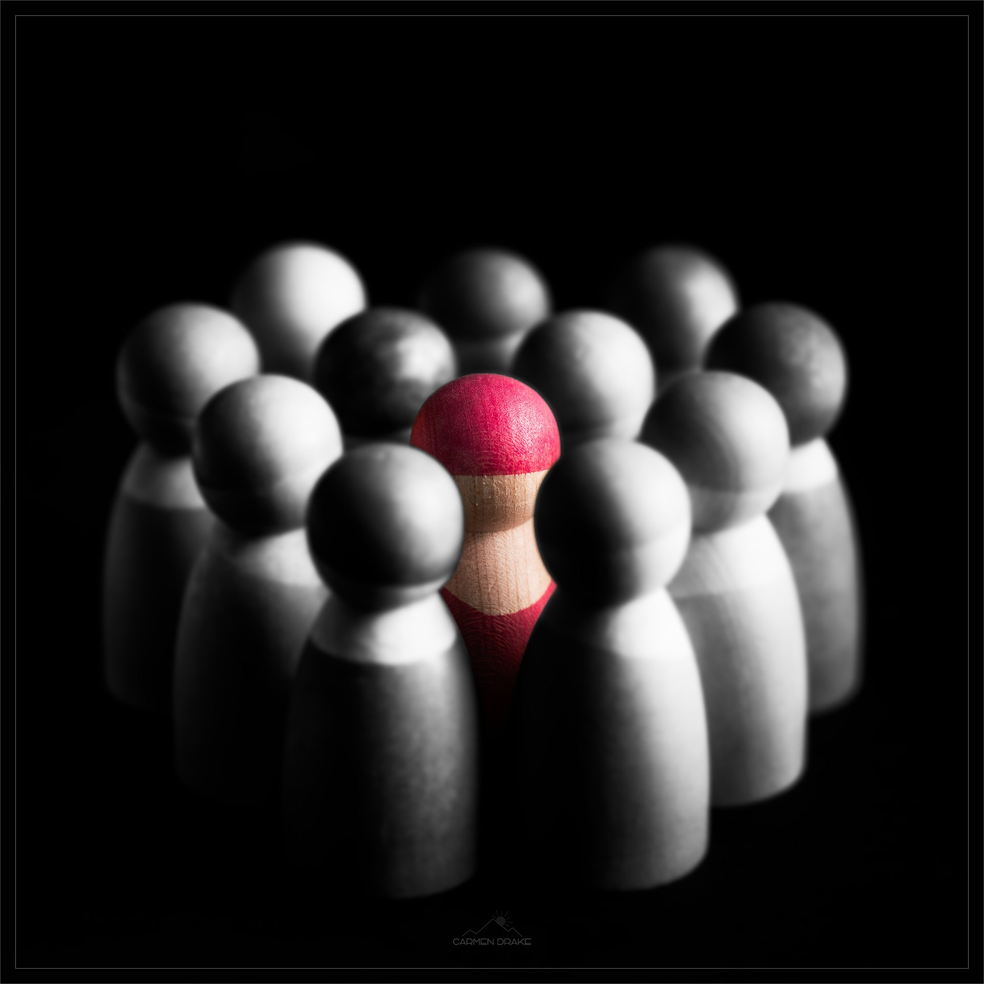 Group of black and white wooden figurines with one red figurine in the center, standing out.