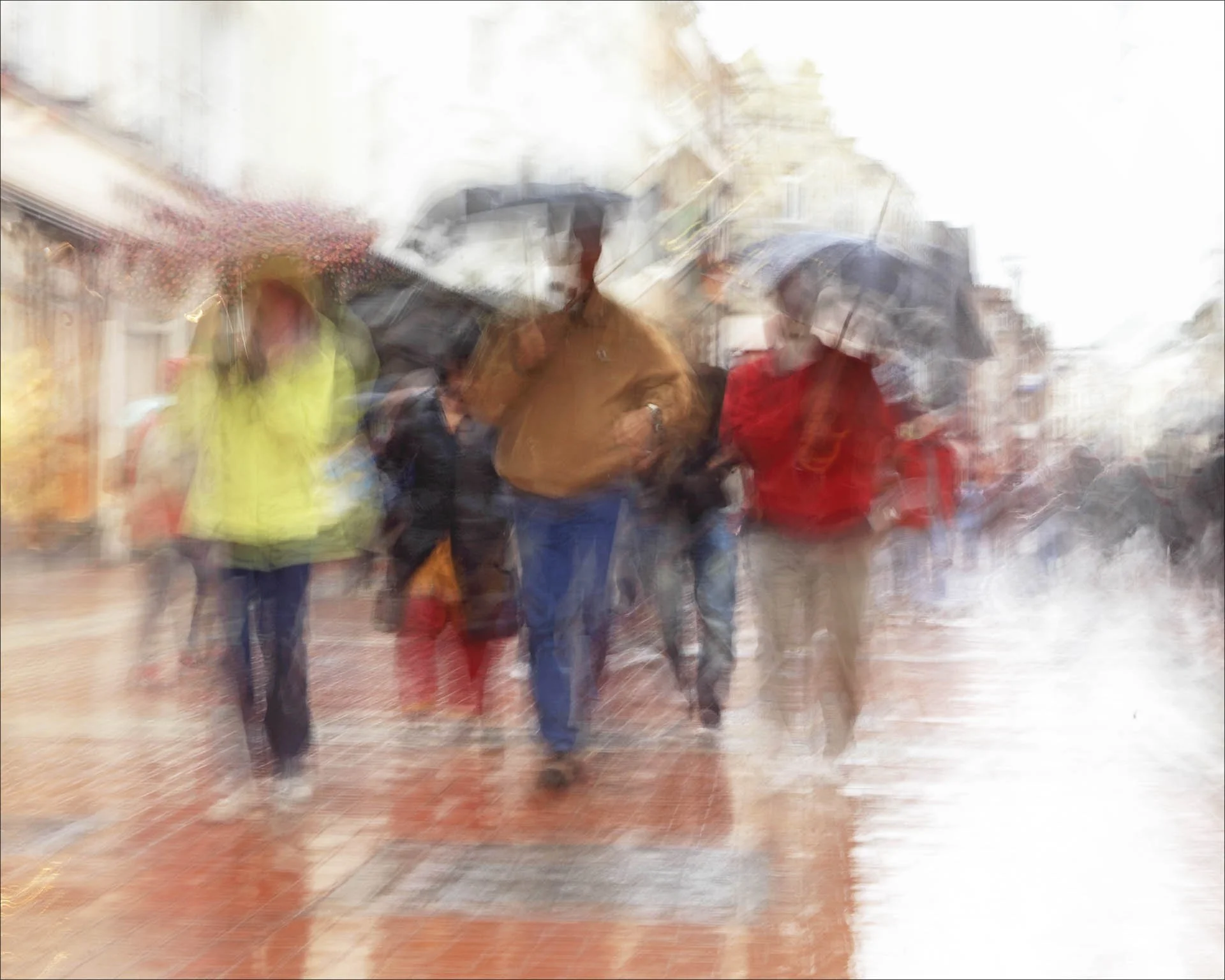 Blurry street scene with people holding umbrellas in the rain.