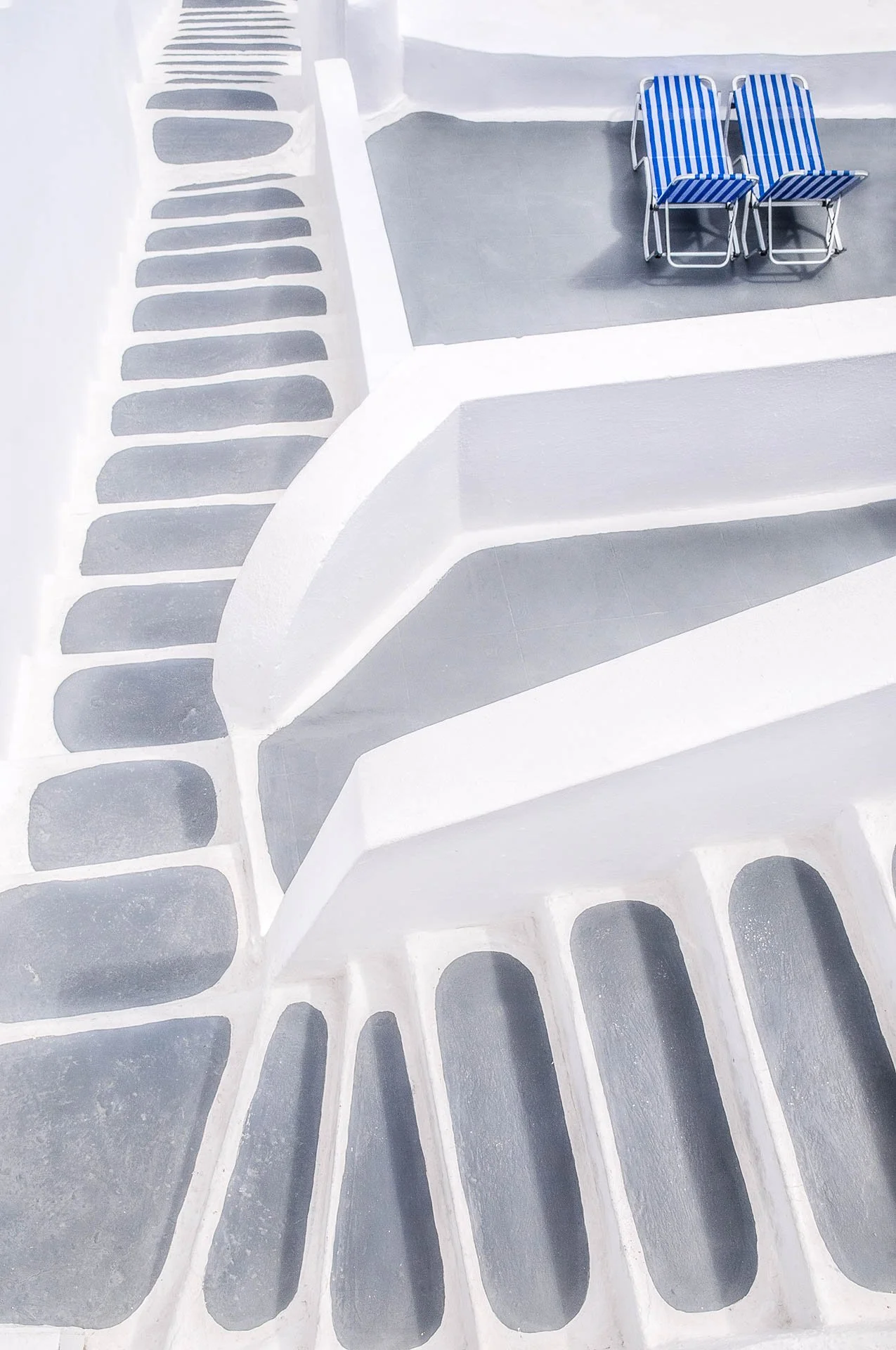 Abstract geometric architectural design with white stairs and blue-striped beach chairs on a gray platform.