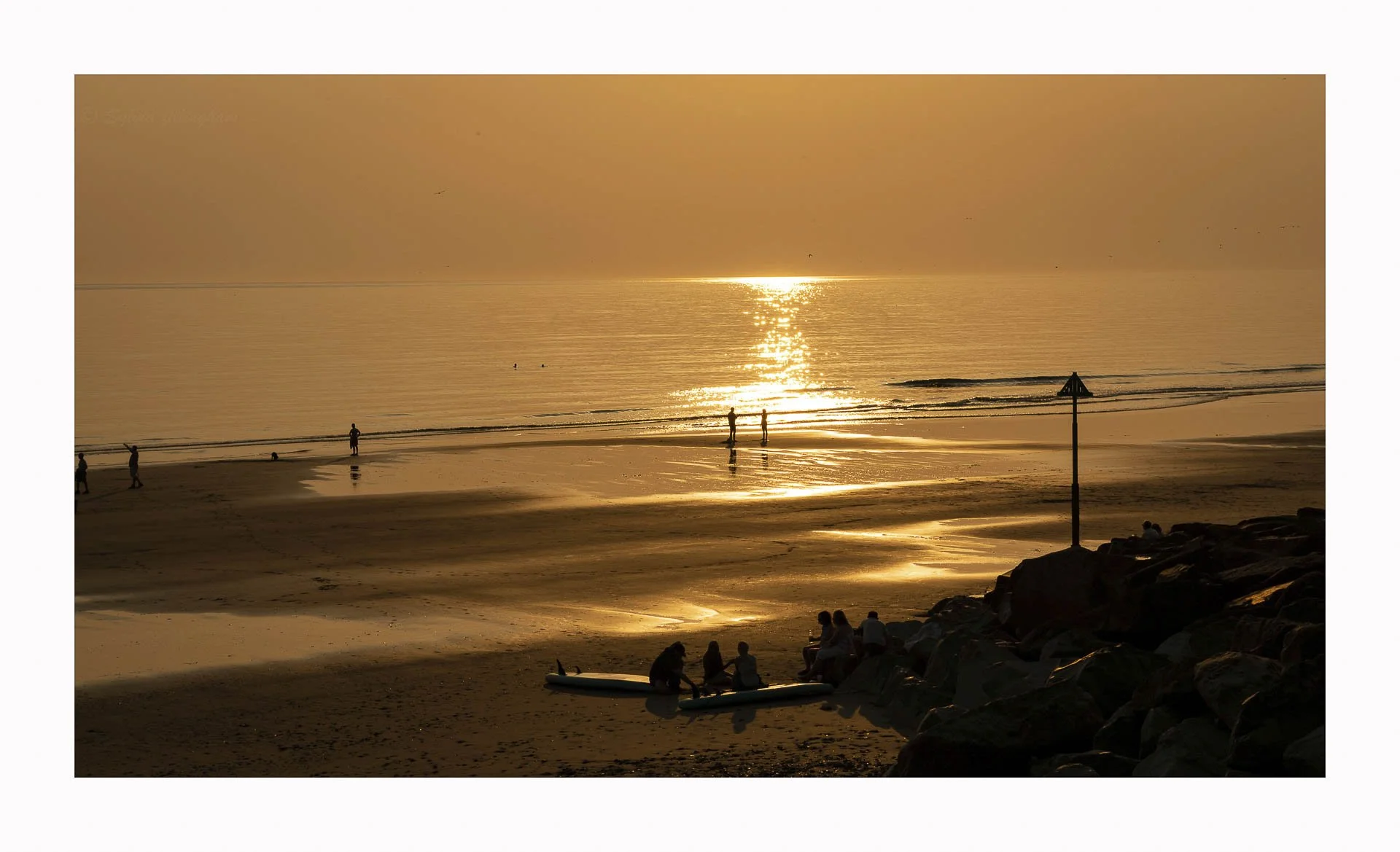 Beach at sunset with people on sand and calm sea