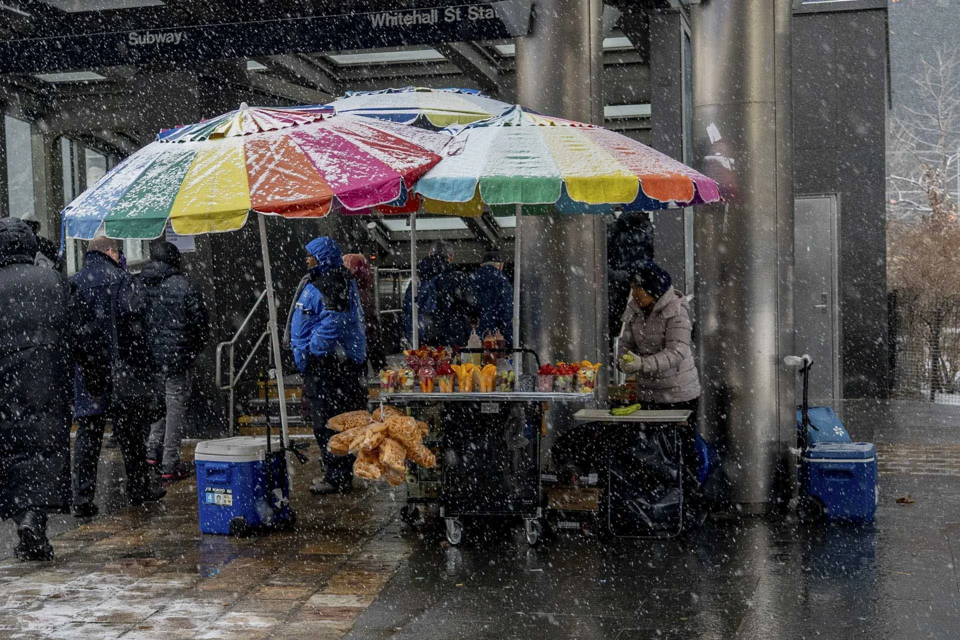  Image credit: Ellen Speiser  (World Food Photography Awards 2025 Street Food shortlist). Street vendors continue selling mangos and other fruit, even in a snowstorm in New York City. The tropical colours of the fruits and umbrellas contrast with the dark winter colours of the commuters, as they hurry through the snow to get indoors. 
