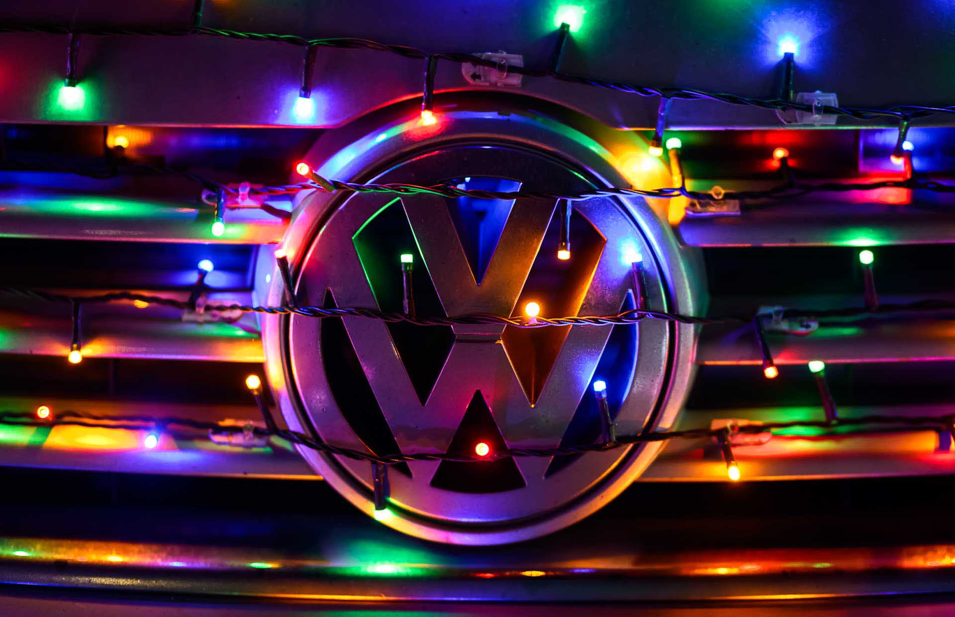 Volkswagen emblem wrapped in multicolored string lights, glowing against a dark background.