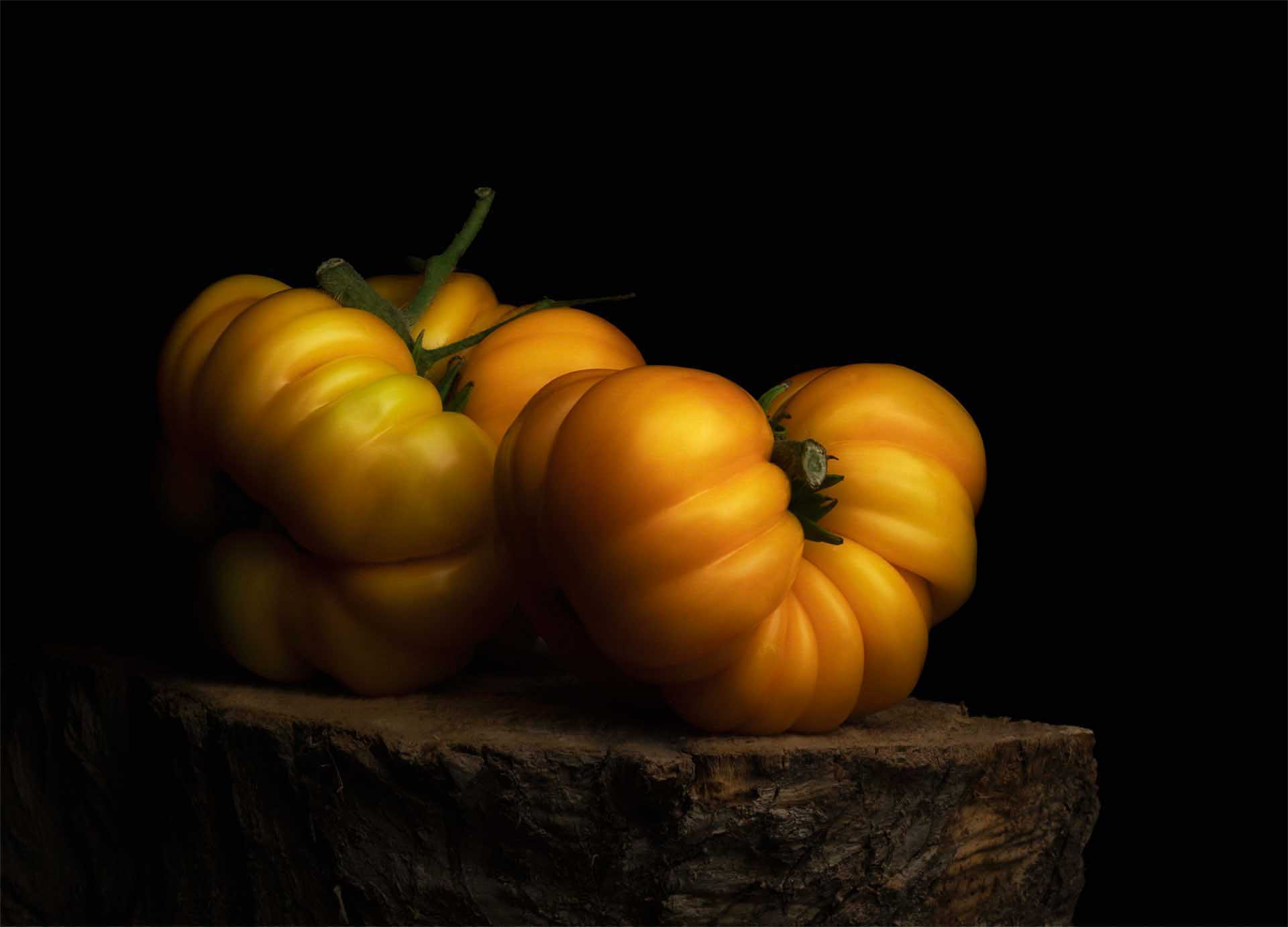 Cluster of ribbed yellow tomatoes resting on a rough stone surface against a black background, dramatic low-key lighting.