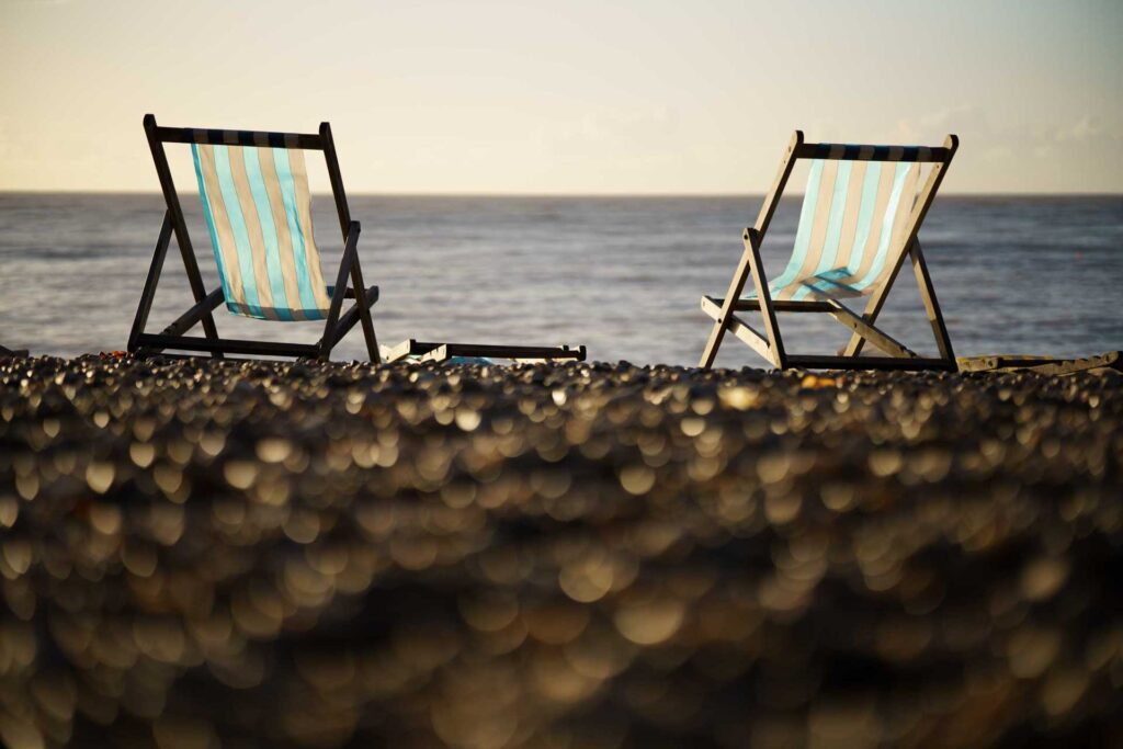 Two striped deck chairs on a pebble beach facing the sea, shot low with soft focus stones in the foreground.