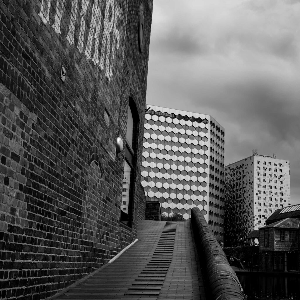 Brick walkway beside a Birmingham canal leading toward modern buildings under an overcast sky.